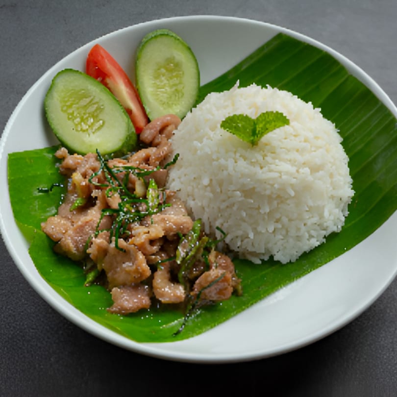 Grace ThaiNY's stir-fried pork with rice, garnished with cucumber, tomato, and mint on a banana leaf.